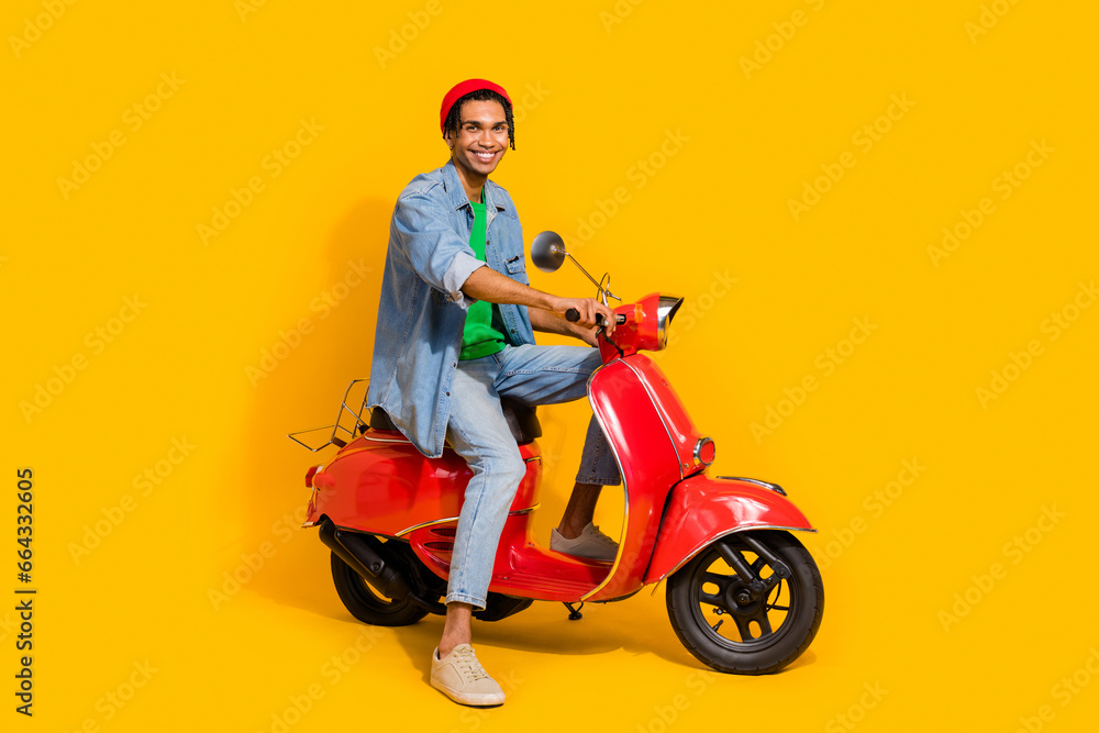 Full size photo of nice young guy riding red vintage motorcycle wear trendy jeans outfit isolated on yellow color background