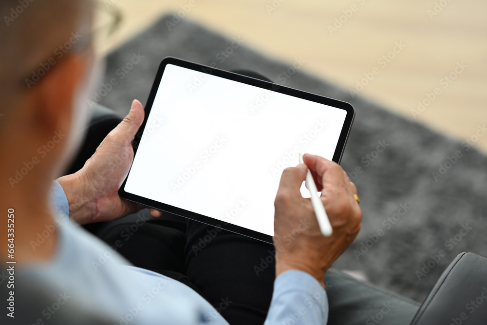 Over shoulder mature man using stylus pen writing on digital tablet. Elderly lifestyle and technology concept Over shoulder mature man using stylus pen writing on digital tablet. Elderly lifestyle and technology concept