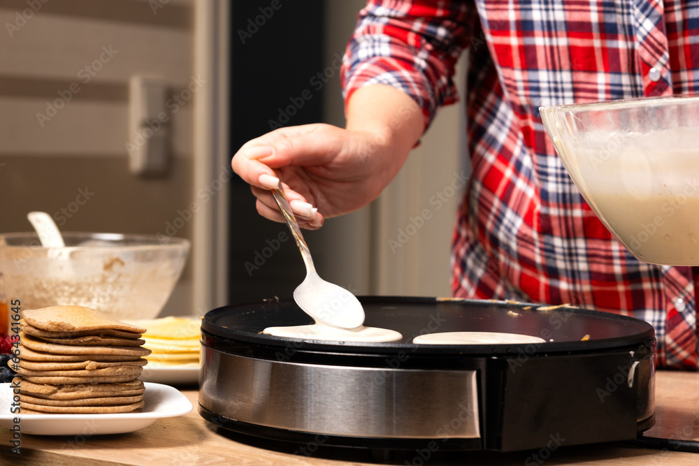 Woman cooking delicious crepe on electric pancake maker in kitchen, closeup - obrazy, fototapety, plakaty 