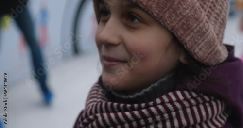 Extreme close-up hand of mother taking care of a Caucasian girl in warm scarf and jacket in winter, straightening her pink knitted hat at the skating rink. It's frosty outside,happy child is smiling