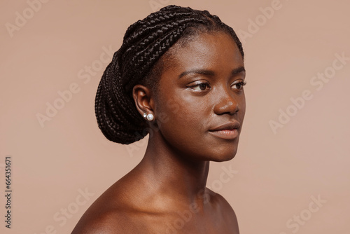 Side view beauty portrait of african young woman with clean healthy skin over beige background. Female with black braided hair, top knot hairstyle.