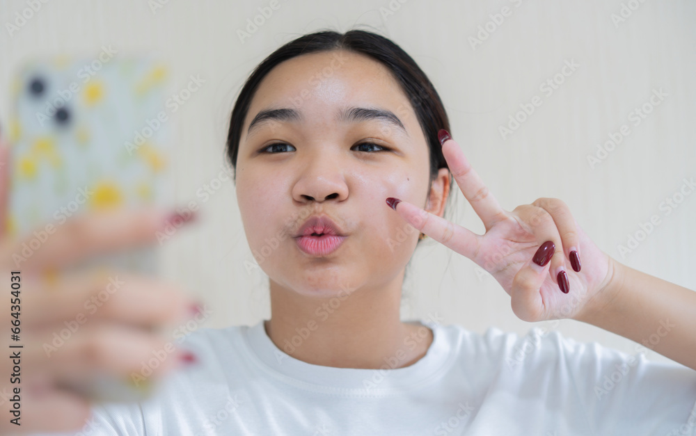 Image of beautiful young Asian girl laughing and showing peace sign while taking selfie photo Image of beautiful young Asian girl laughing and showing peace sign while taking selfie photo