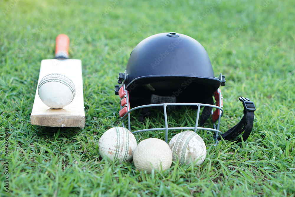 Cricket kits, helmet, cricket balls and bat on grass field. Concept