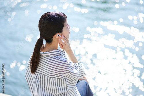 川辺でワイヤレスイヤホンで音楽を聴く日本人の女性 #664369641