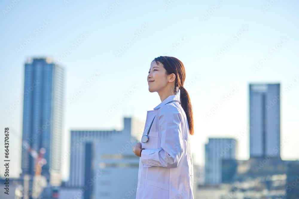 ビジネス街の町並みと白衣を着た日本人の女性医師 ビジネス街の町並みと白衣を着た日本人の女性医師