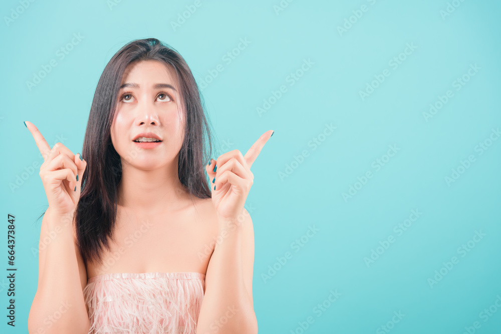 Asian happy portrait beautiful young woman standing her pointer finger up isolated on blue background with copy space for text Asian happy portrait beautiful young woman standing her pointer finger up isolated on blue background with copy space for text