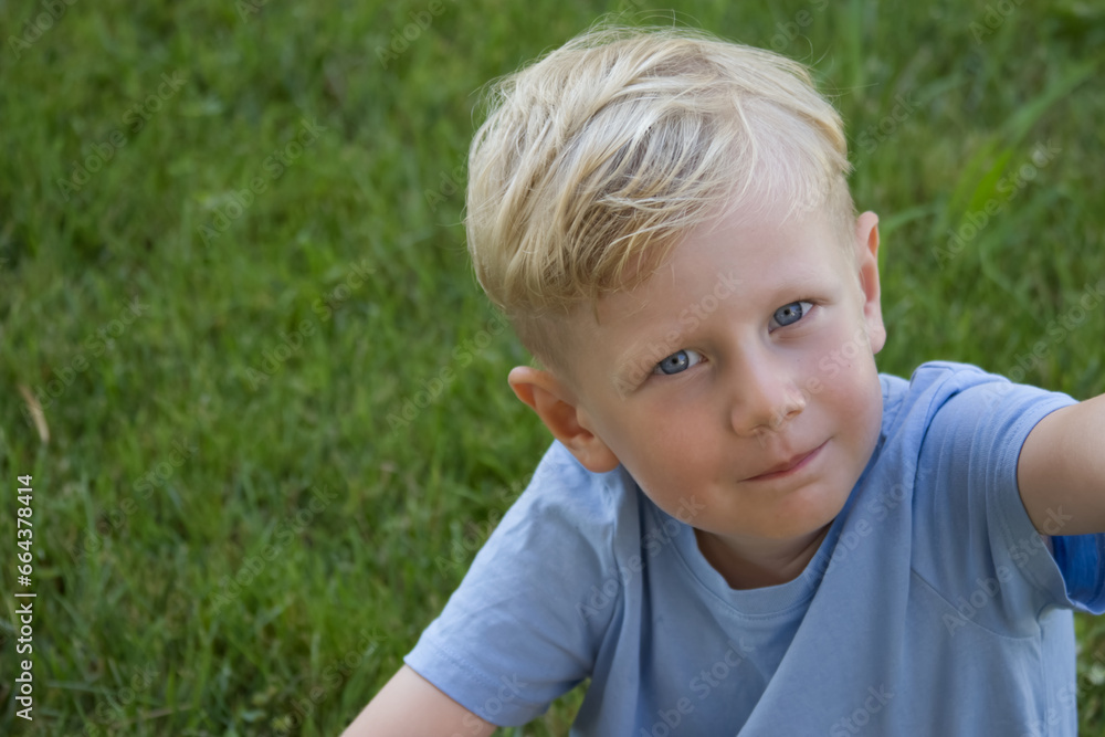 Portrait of a fair-haired boy looking at the camera against a background of a green lawn Portrait of a fair-haired boy looking at the camera against a background of a green lawn