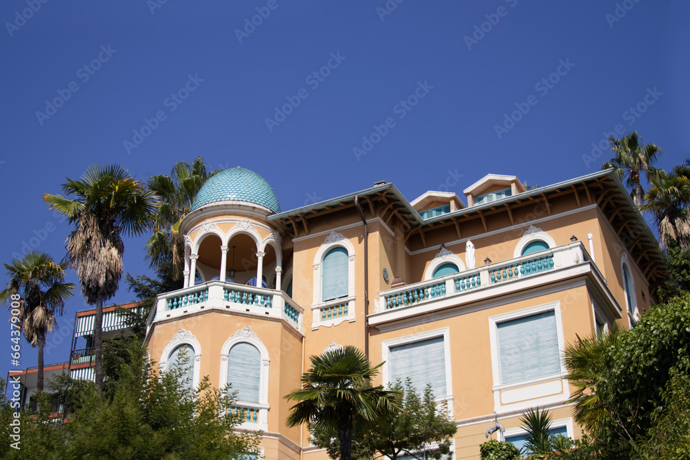 View of an ancient Italian villa surrounded by a green flowering garden and palm trees View of an ancient Italian villa surrounded by a green flowering garden and palm trees