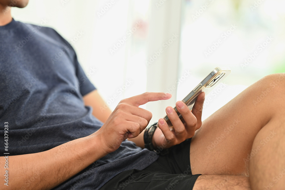 Young man sitting on couch and using smartphone, typing message or posting in social media