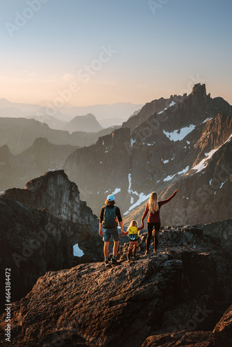 Family hiking travel in Norway mountains: parents and child with backpacks on the top adventure healthy lifestyle outdoor active vacations together mother and father with kid climbing