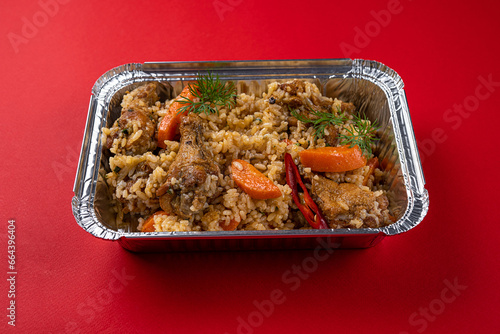 Boiled Rice with Chicken and Carrots in a Disposable Foil Box on a Red Background