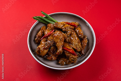 Chicken Drumsticks and Wings in Spicy Teriyaki Sauce with Sesame Seeds on a Gray Plate on a Red Background