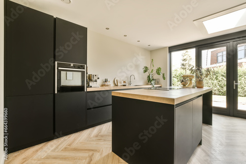 a modern kitchen with black cabinetry and wood flooring in an open plan living room, dining area on the other side