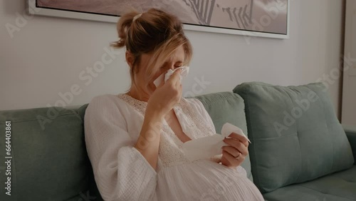 Pregnant woman trying to sneeze while having a sore throat sitting at home. Sick expectant mother catching a cold. Healthcare and pregnancy concept.