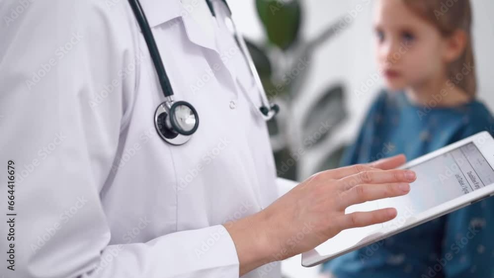 Doctor and patient in the clinic. Pediatrician is using a tablet pc while a little fair-haired girl is sitting at the background. Medicine, healthcare concepts