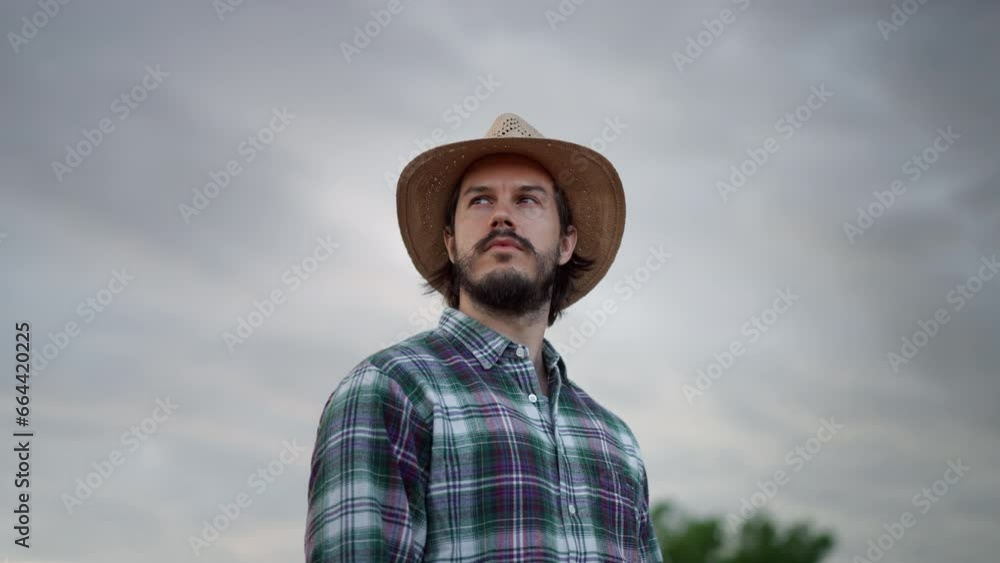 Man in plaid shirt holding spikelet, reed, dry grass his mouth and looking away while standing Man in plaid shirt holding spikelet, reed, dry grass his mouth and looking away while standing