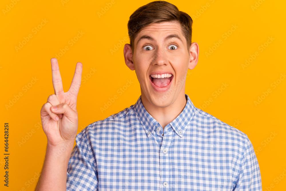 Photo of young smiling good mood brunet hair guy after barber shop showing v-sign isolated on yellow color background Photo of young smiling good mood brunet hair guy after barber shop showing v-sign isolated on yellow color background