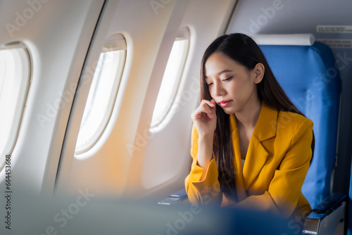 Young asian chinese airplane passenger woman experiencing discomfort, Airplane headache. Worried female passenger holding head, feeling unwell Anxiety and fear in the skies. Stressful travel moments. photo