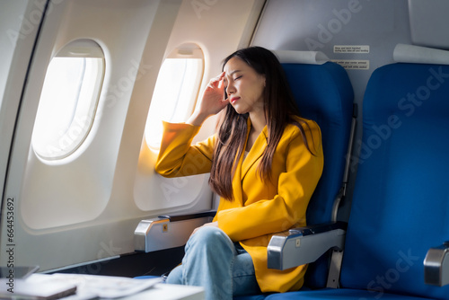 Young asian chinese airplane passenger woman experiencing discomfort, Airplane headache. Worried female passenger holding head, feeling unwell Anxiety and fear in the skies. Stressful travel moments.