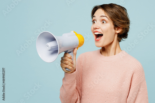 Young woman she wear beige knitted sweater casual clothes hold in hand megaphone scream announces discounts sale Hurry up isolated on plain pastel light blue cyan background studio. Lifestyle concept.