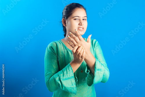 Portrait of an Indian women holding her palm with painful grimace in blue background