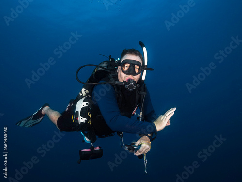Closeup of a male scuba diver in the deep blue sea looking at the camera showing the ok signal