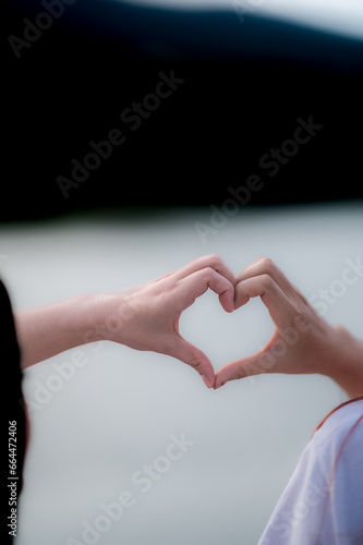 young woman and her friend raised their hands together to form heart shape to show their friendship love and kindness with their belief and power of faith in their friendship. concept of friendship photo