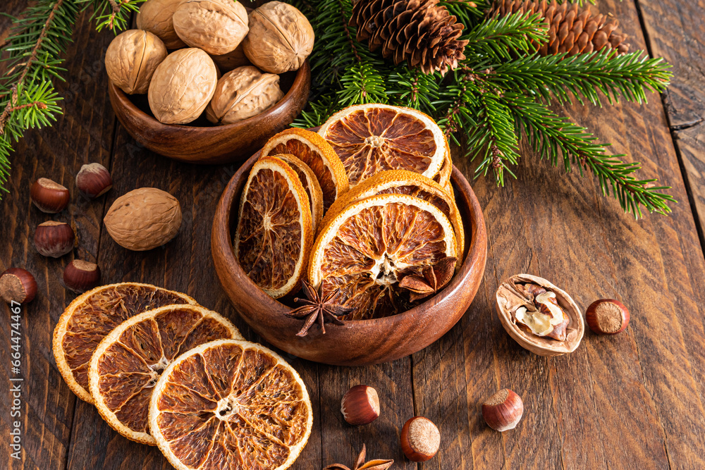 Natural Christmas decorations. Dried orange slices in a wooden bowl on a rustic table with green spruce branches, cones, nuts. Rustic style