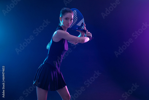 Padel tennis player with racket on tournament. Girl athlete with paddle racket on court with neon colors. Sport concept. Download a high quality photo for design of a sports app or tour events. photo