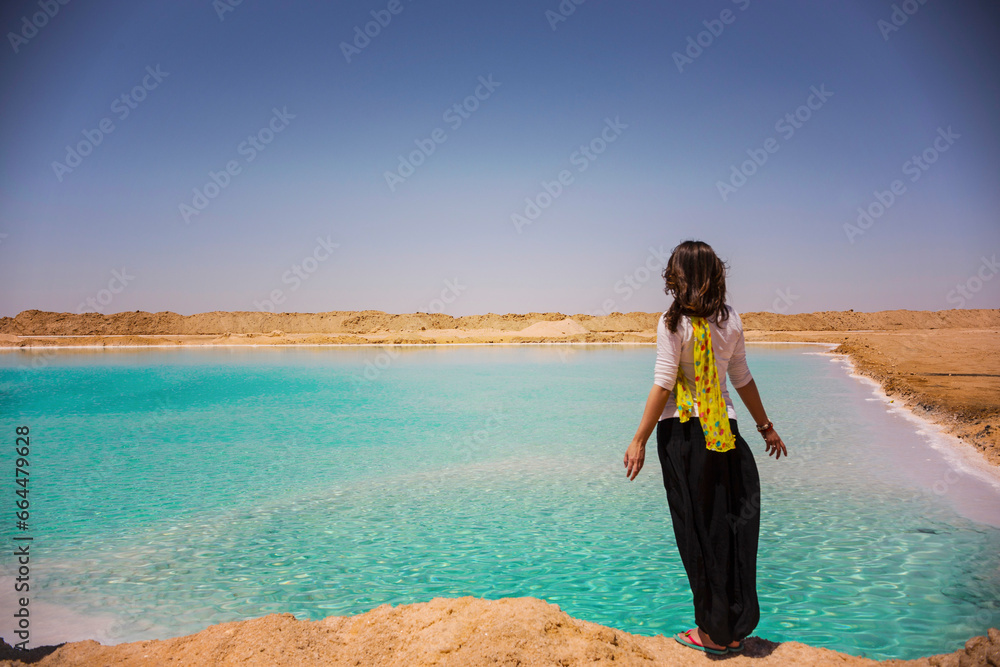 Young woman (back view) on the shore of salt lake in Siwa oasis, salty lake with turquoise water, Egypt
