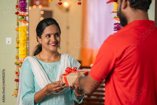 Happy excited indian girl receiving box from delivery person during diwali festive gifting - concept of online or ecommerce shopping, doorstep delivery and special occasion.