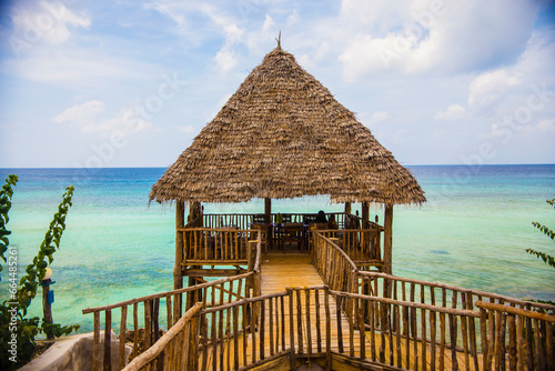 Fototapeta Naklejka Na Ścianę i Meble -   Wooden pavilion with palm leaves roof against turquoise water background, Zanzibar
