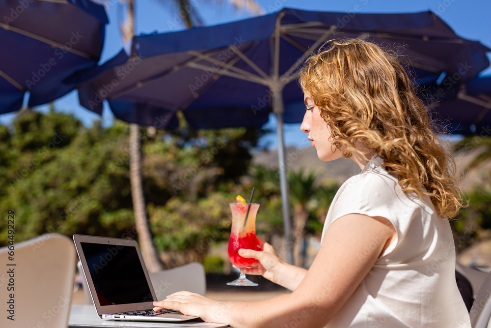 Fototapeta premium Tourist girl using a laptop on summer vacation in a snack bar terrace on the beach