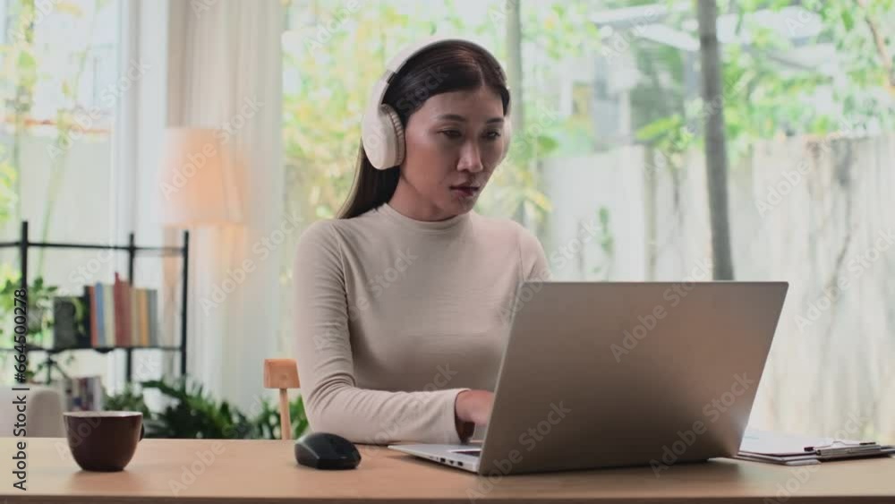 Medium shot of young female entrepreneur in headphones working on laptop from home, sitting at desk with cup of tea Medium shot of young female entrepreneur in headphones working on laptop from home, sitting at desk with cup of tea