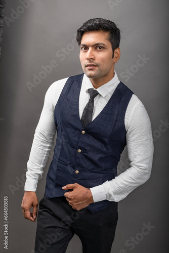 Studio shot of cheerful, young, handsome Indian business man in formal wear against grey background. Corporate male model. Fashion Portrait.