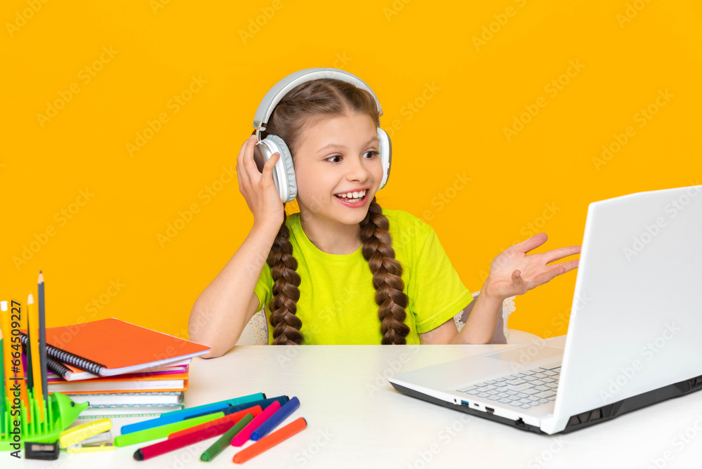 Online education. A little girl communicates with a teacher remotely using a laptop. A child with headphones is looking at a computer monitor. Online education. A little girl communicates with a teacher remotely using a laptop. A child with headphones is looking at a computer monitor.