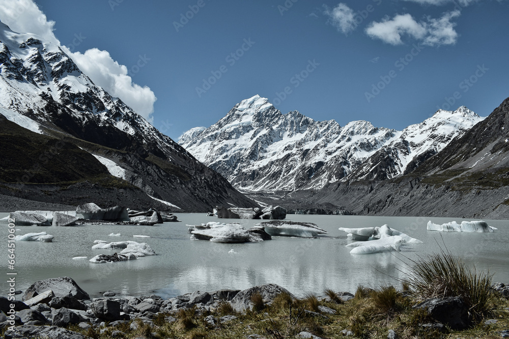 Obraz premium The majestic Mount Cook in New Zealand, a glacial lake, a bright blue sky, snow and icebergs floating in the water - a spectacular and frosty scenery.