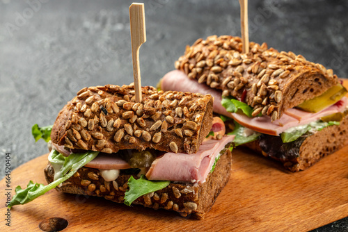 Two delicious ham sandwiches with pickled cucumbers served on a wooden board