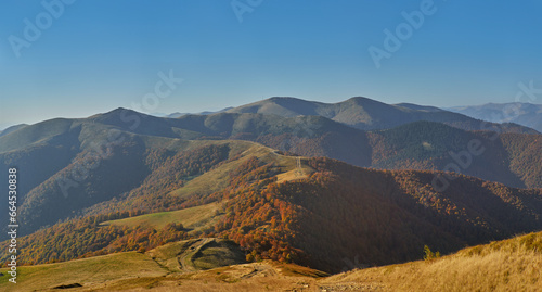 Panorama of autumn mountain landscape in the evening. A dirt road along the top of the ridge, through beech groves with golden foliage and mountain pastures. The beauty of the autumn Carpathians