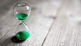 Hourglass with green sand time passing background concept for business deadline, urgency and running out of time