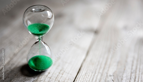 Hourglass with green sand time passing background concept for business deadline, urgency and running out of time photo