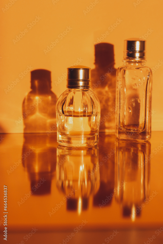 Glass miniature bottles with perfume, essential oils with reflections Cosmetic products. Facial and body skin care, beauty shop concept. Women's grooming products on orange vertical background. Glass miniature bottles with perfume, essential oils with reflections Cosmetic products. Facial and body skin care, beauty shop concept. Women's grooming products on orange vertical background.