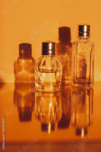 Glass miniature bottles with perfume, essential oils with reflections Cosmetic products. Facial and body skin care, beauty shop concept. Women's grooming products on orange vertical background.