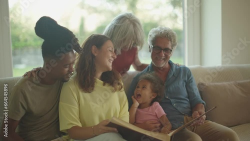 young married multiethnic couple with daughter at grandparents home looking together to old family photo album