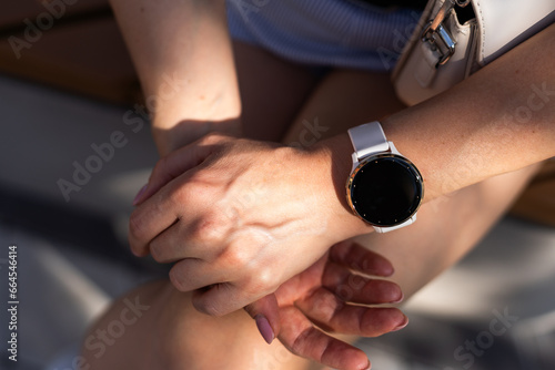 Woman hand wearing a smartwatch and checking active lifestyle and using fitness tracker outdoor on the beach.