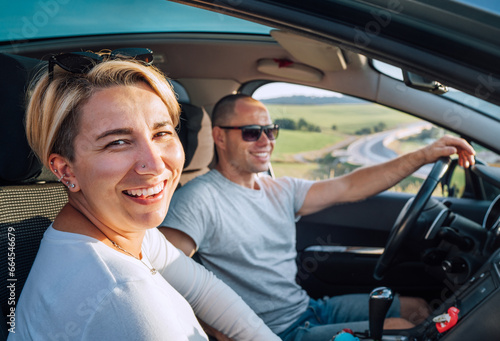 Portrait of cheerful smiling young woman with husband have auto journey inside modern car. Safety riding car, car sharing and traveling concept image. © Soloviova Liudmyla