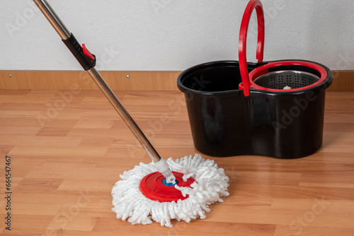 Cleaning concept mop and bucket. Cleaning products and spin mop with red details on the floor in an interior with a wooden floor or parquet, laminate. photo