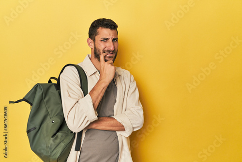 Young Hispanic man with travel backpack relaxed thinking about something looking at a copy space.