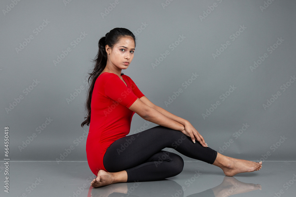 Fototapeta premium Healthy young woman in red t-shirt and black leggings doing yoga and stretching exercises isolated on grey background
