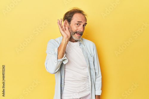 Caucasian middle-aged man in yellow studio trying to listening a gossip.